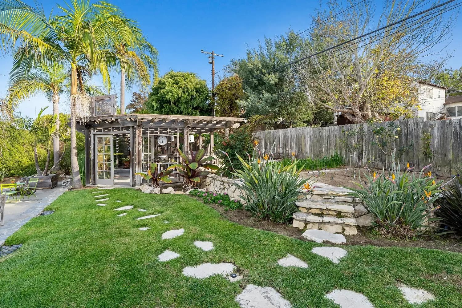 Backyard garden with flagstone path, stone planter bed, and pergola-covered patio