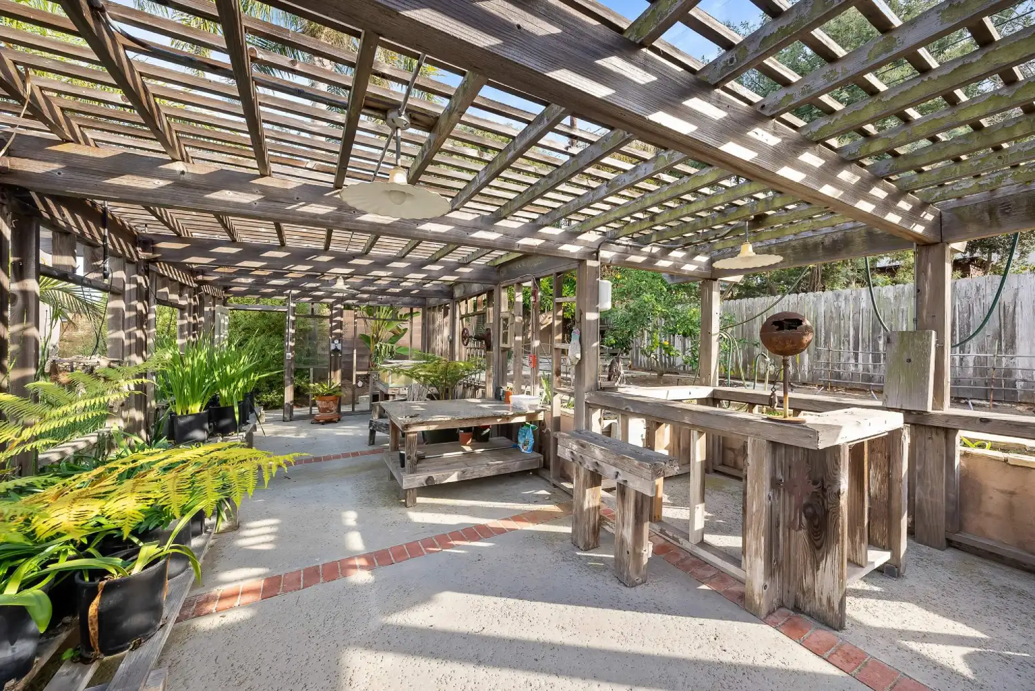 Expansive timber pergola sheltering a potting workspace and gravel patio with brick inlay