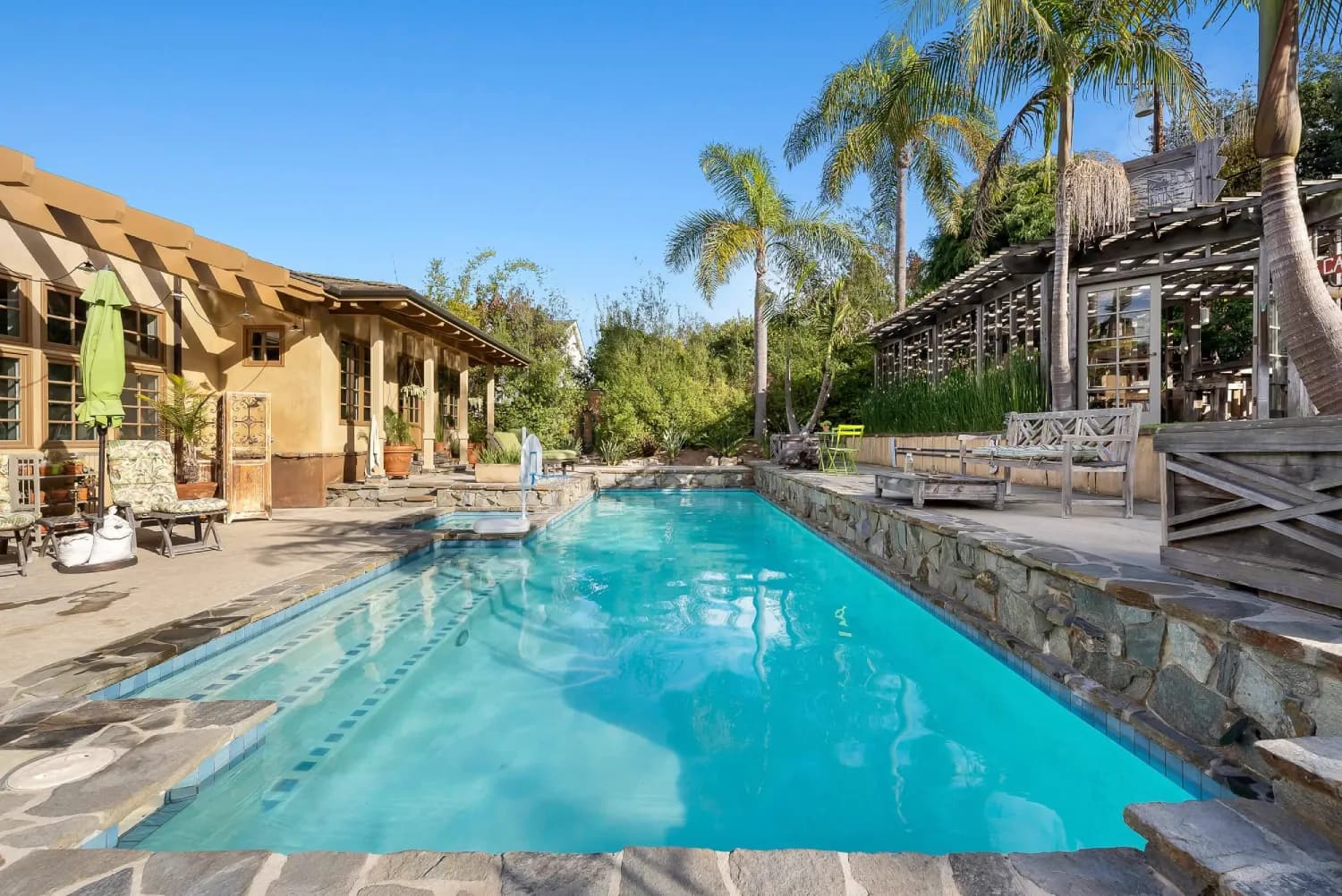 Custom pool with stone-clad surround, flagstone deck, and palm-shaded patio seating