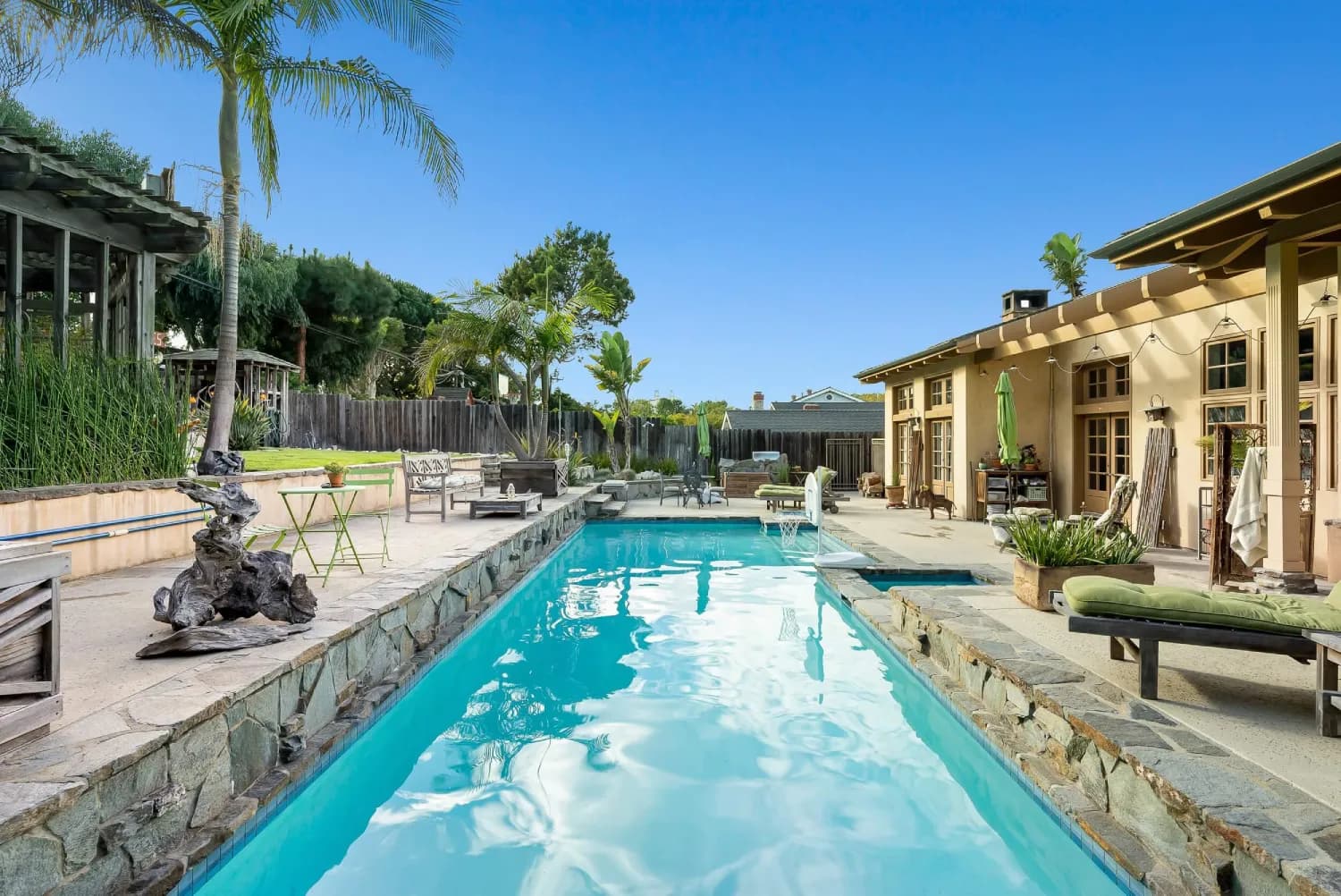 Lap pool with raised stone wall and lounge chairs beside the patio