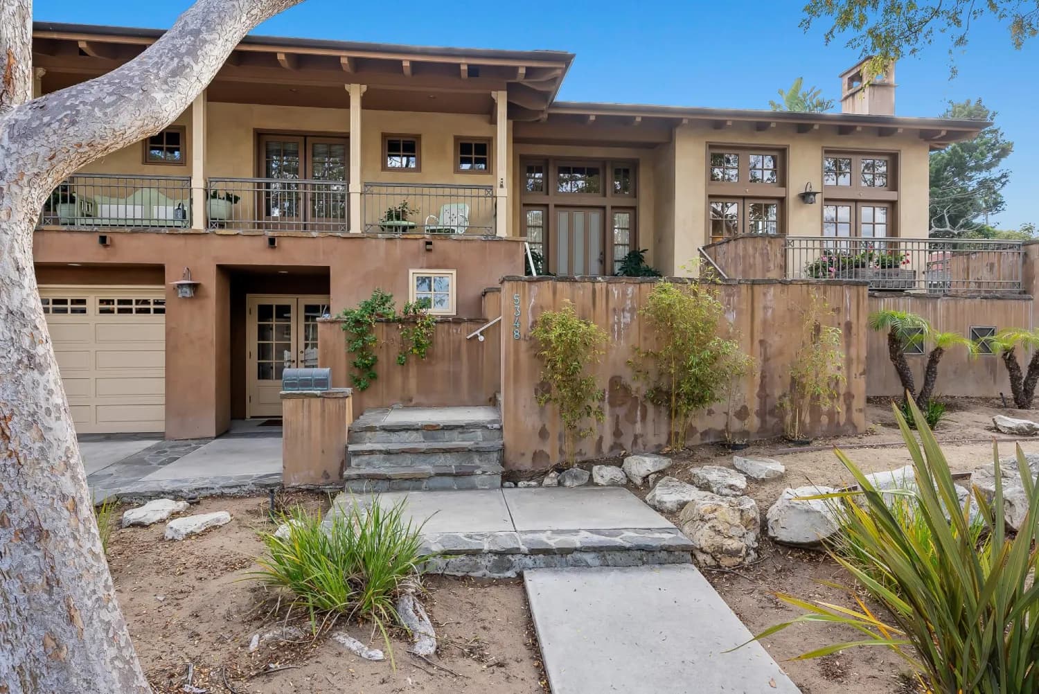Front entry with stucco retaining wall, stone steps, and columned upper balcony