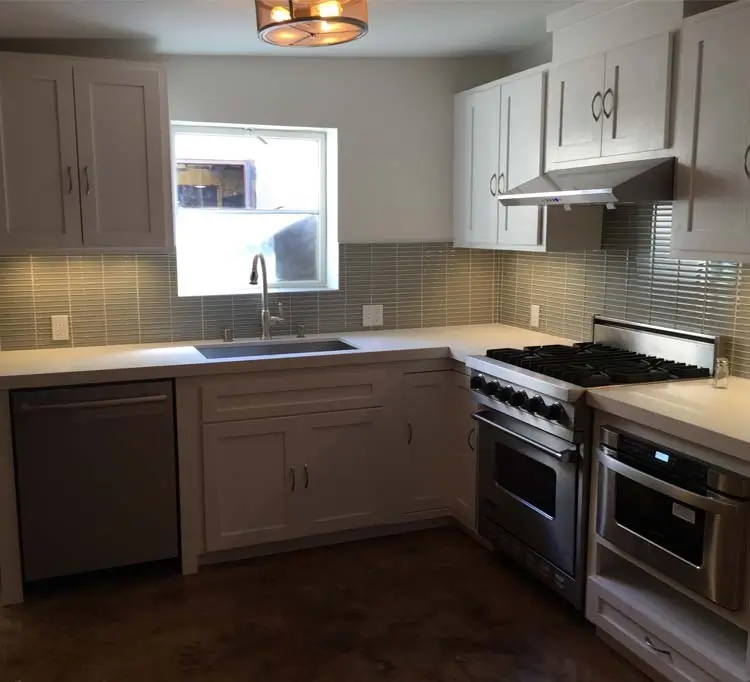 L-shaped loft kitchen with glass-tile backsplash, gas range, and white quartz counters at Marcelina Lofts