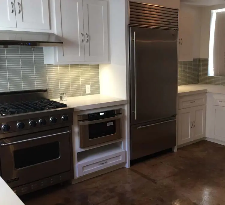 Stainless gas range and built-in refrigerator beside white cabinetry in a Marcelina Lofts kitchen