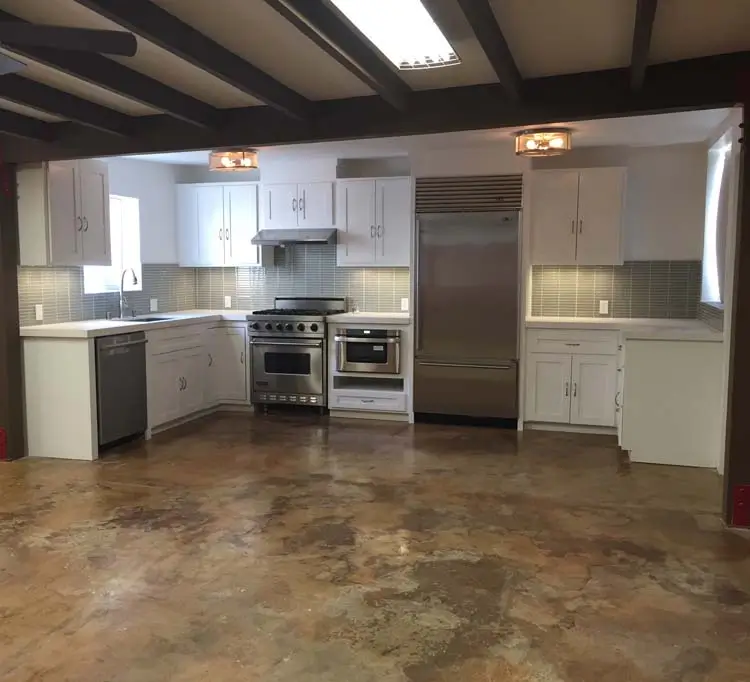 Open loft interior with exposed ceiling beams and stained concrete floor opening to the kitchen