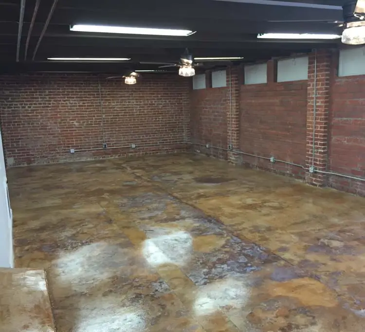Open-plan loft with exposed ceiling beams, white kitchen, and expansive stained concrete floor