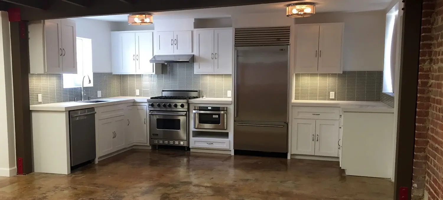 Renovated Marcelina Lofts kitchen with white cabinets, stainless appliances, and stained concrete floor