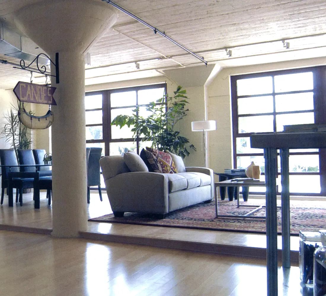 Furnished loft living area with exposed concrete column, plank ceiling, and tall industrial windows at Mission District Lofts