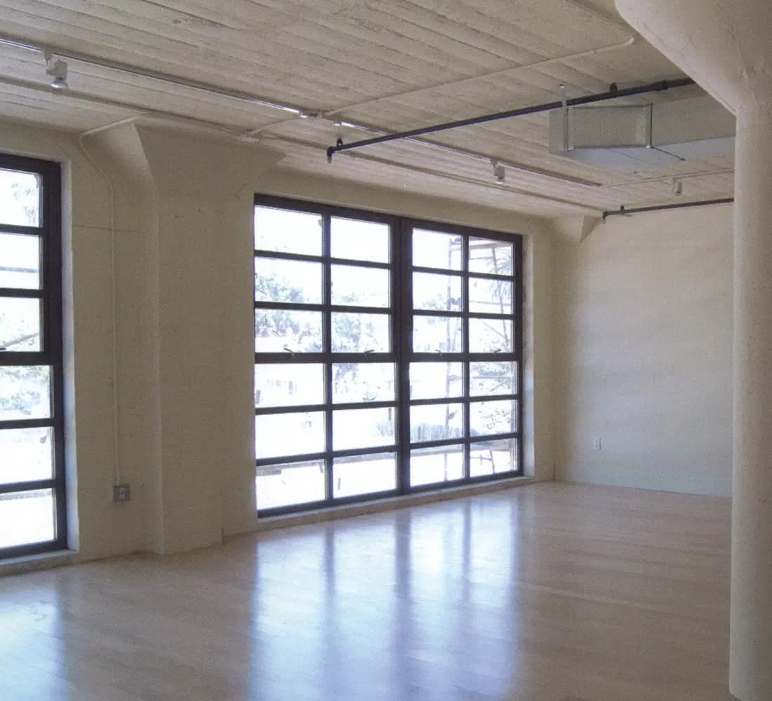 Empty loft interior with concrete columns, wood floors, and saw-cut window walls at Mission District Lofts