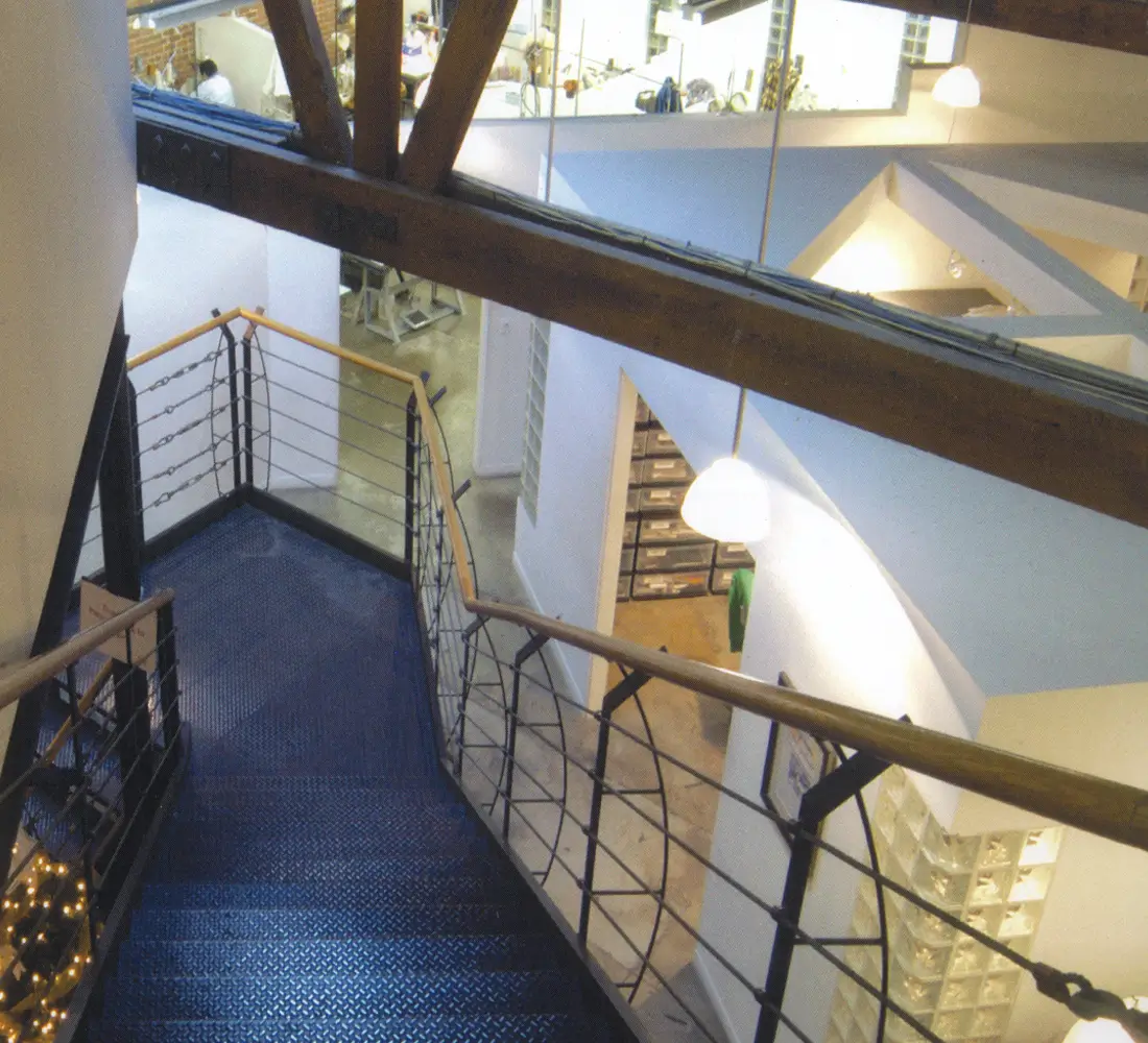 Steel staircase with diamond-plate treads descending past curved trusses to the floor below