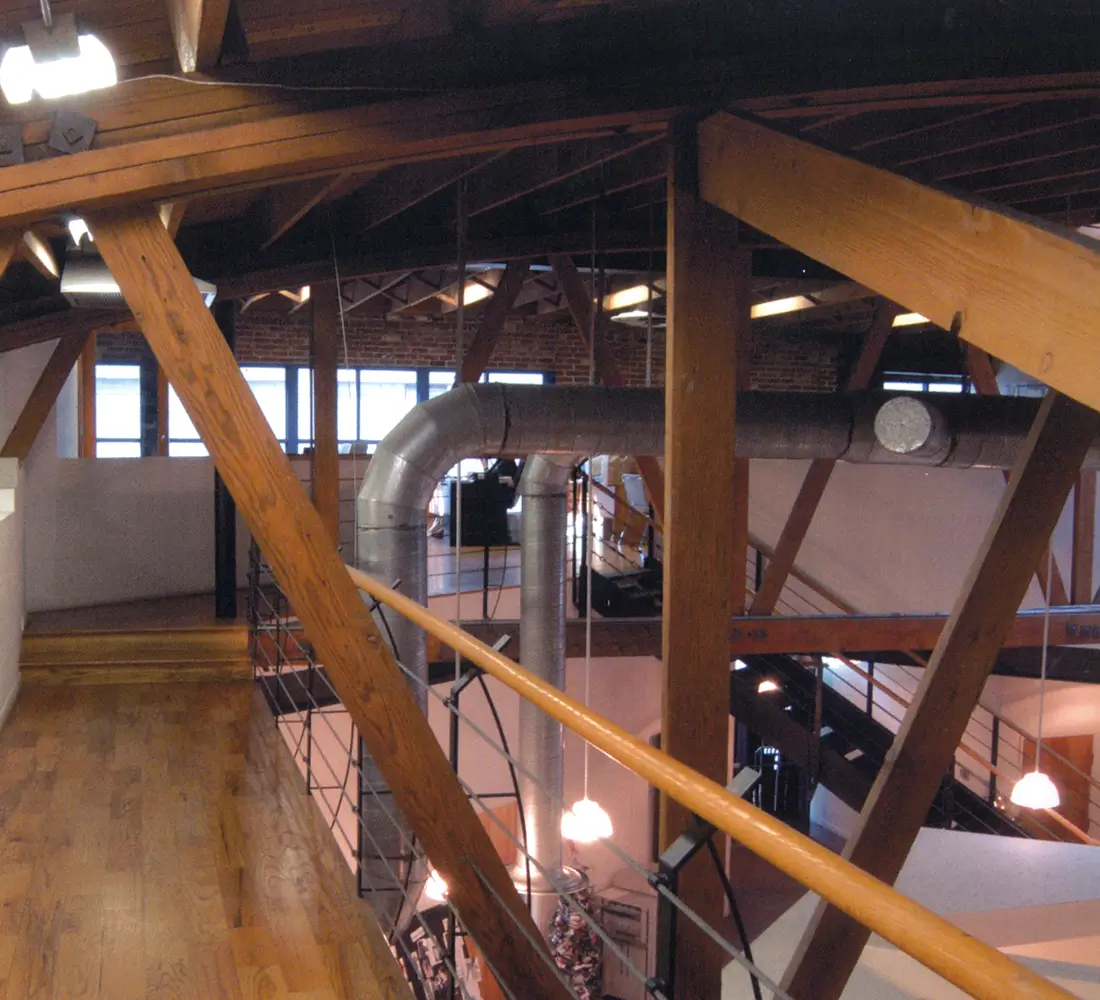 Restored timber bow trusses and exposed ductwork above a wood-floored loft interior