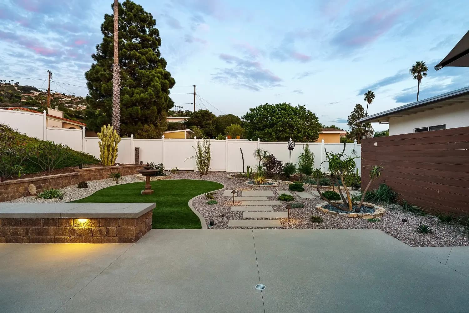 New artificial-turf lawn, stone retaining wall, and paver path with landscape lighting