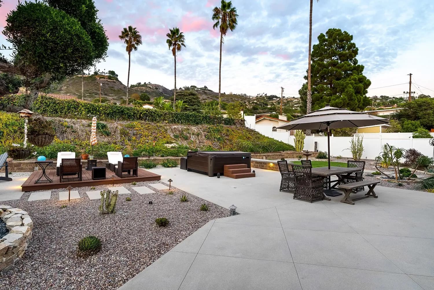 Drought-tolerant backyard with palms, spa, and umbrella dining set framed by South Bay hills