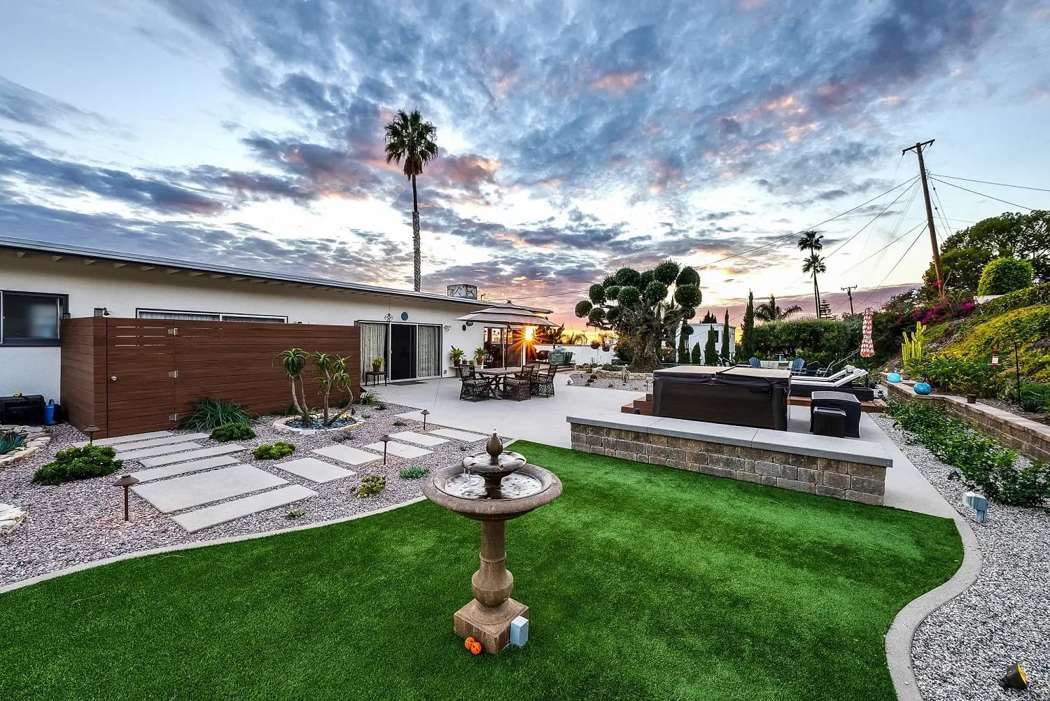 Manicured turf lawn with a stone fountain centerpiece and paver walkway at twilight