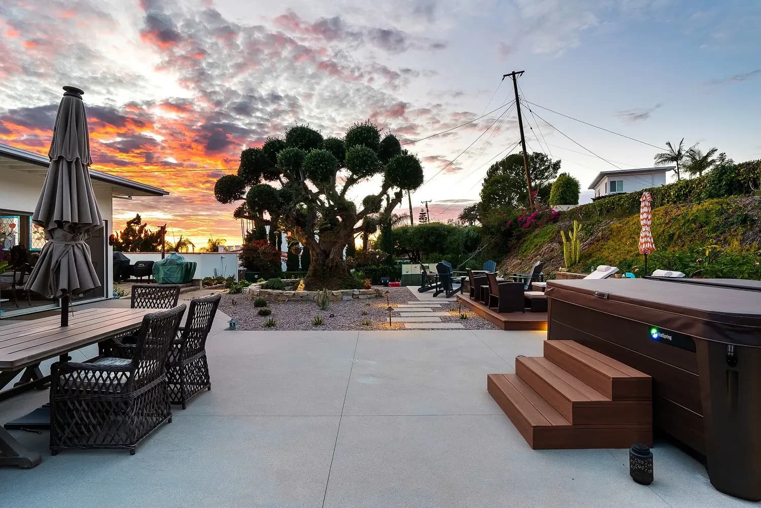 Wide view of the rebuilt backyard with spa, deck, and topiary against a vivid sunset
