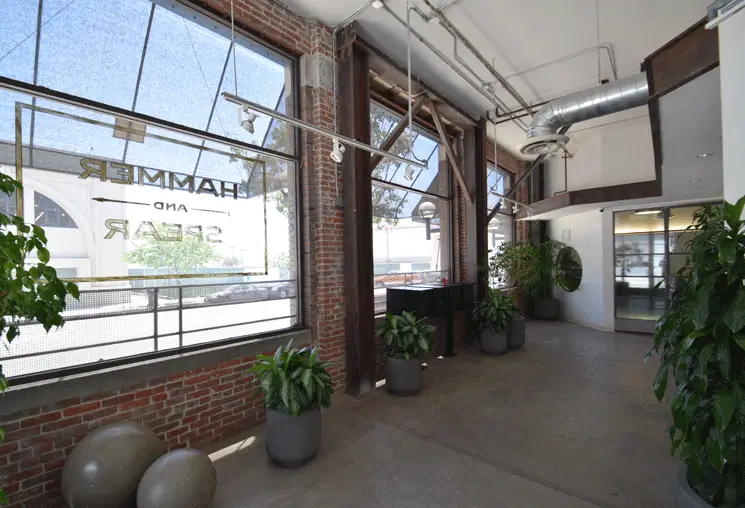 Ground-floor commercial space with tall windows, exposed brick, ductwork, and potted plants at Toy Lofts