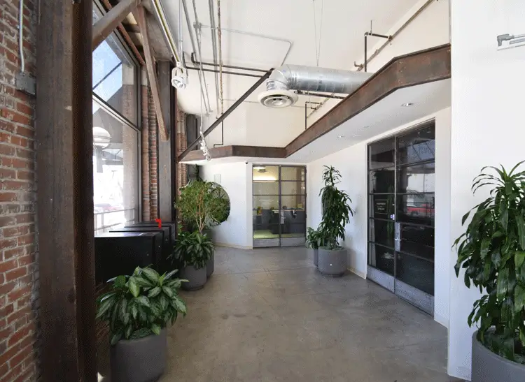 Adaptive-reuse loft lobby with exposed brick, timber columns, polished concrete, and greenery