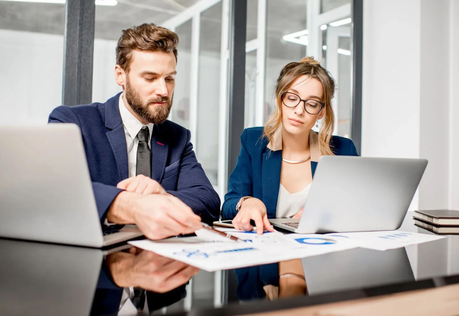 Two business professionals reviewing project charts and laptops in an office