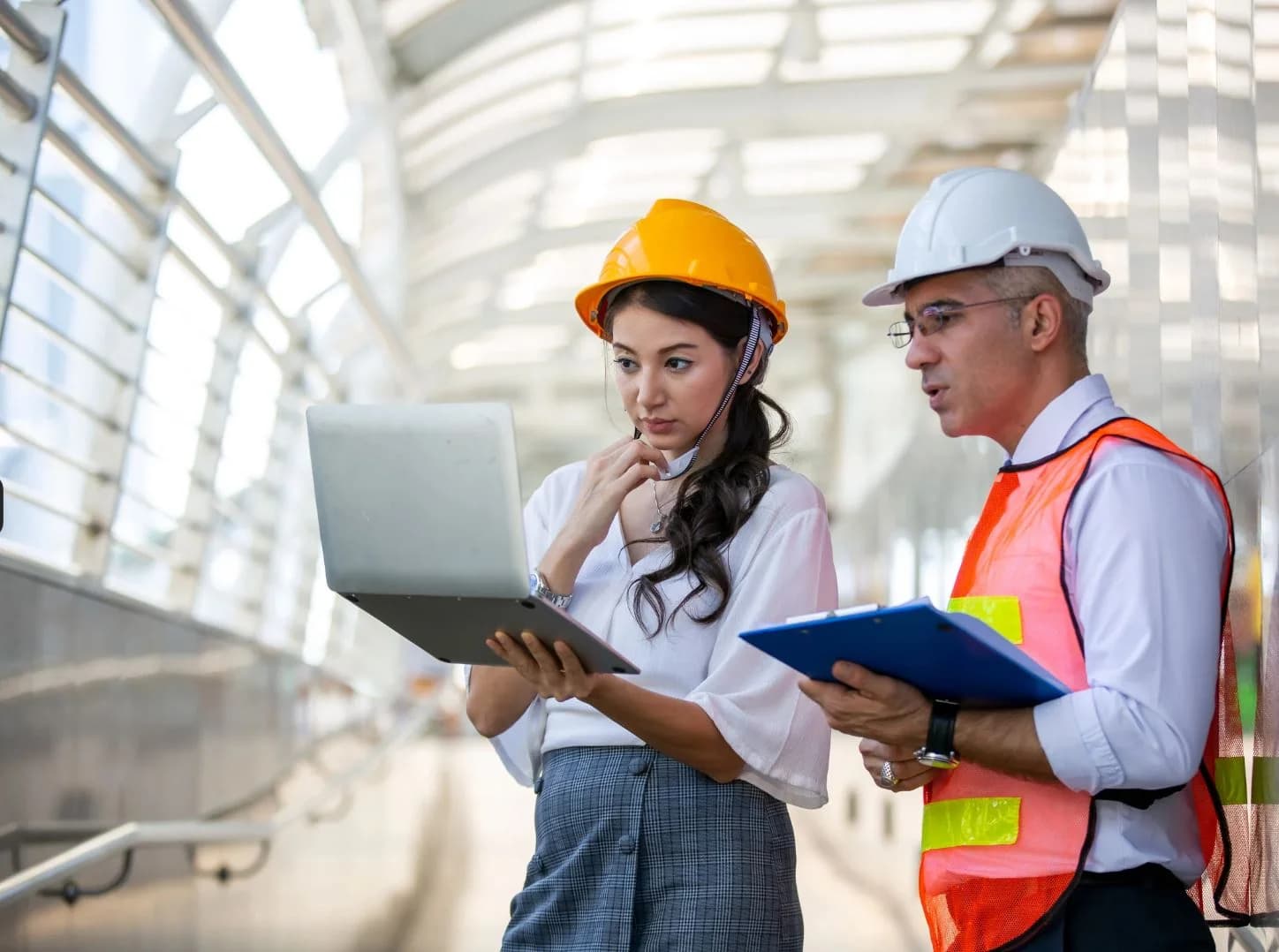 Engineer and project manager in hard hats reviewing a laptop on a new build site