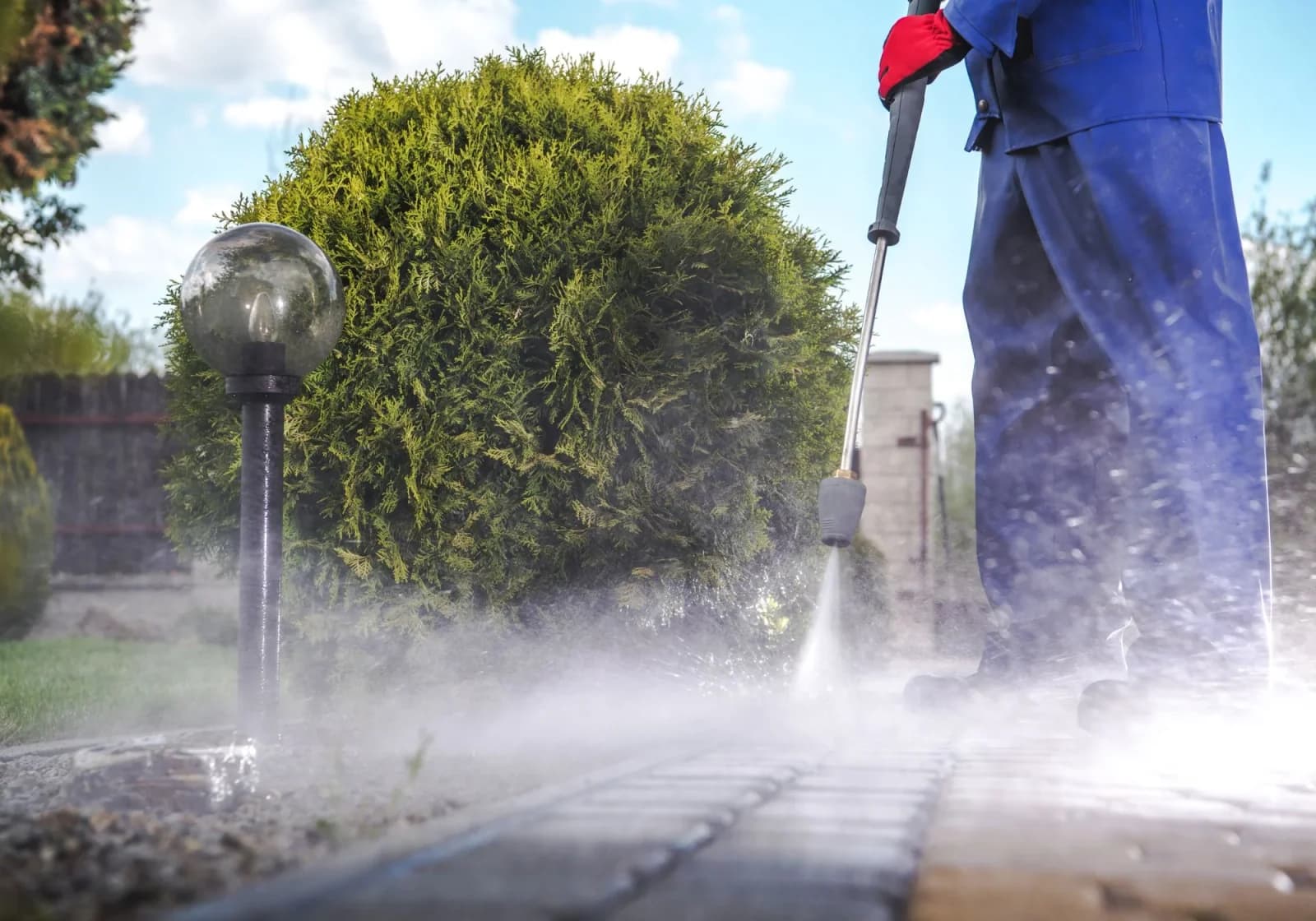 Worker pressure washing a paved walkway, sending up a spray of mist