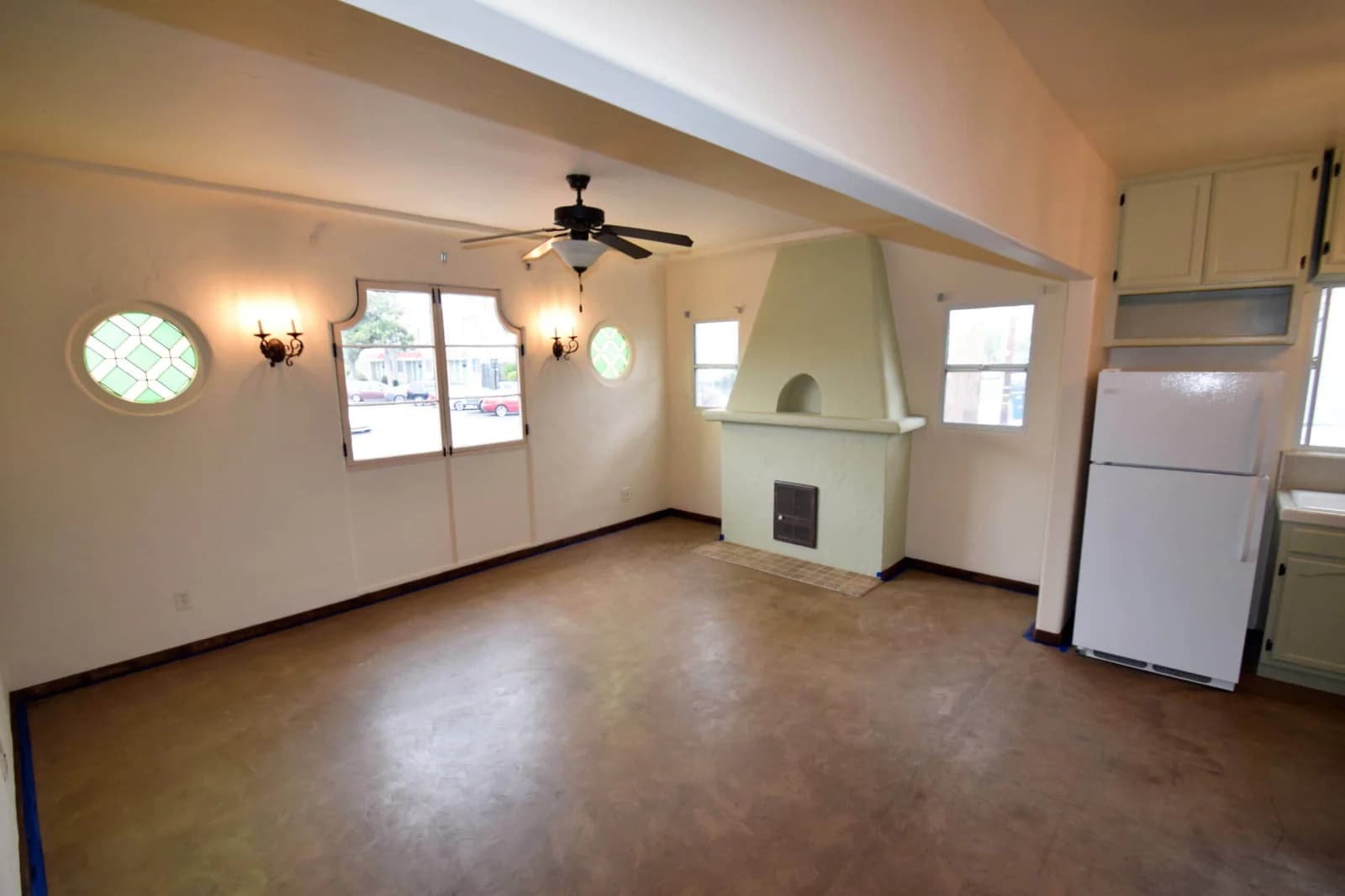 Living room with stucco corner fireplace, stained-glass round windows, and ceiling fan at Broadway Lofts