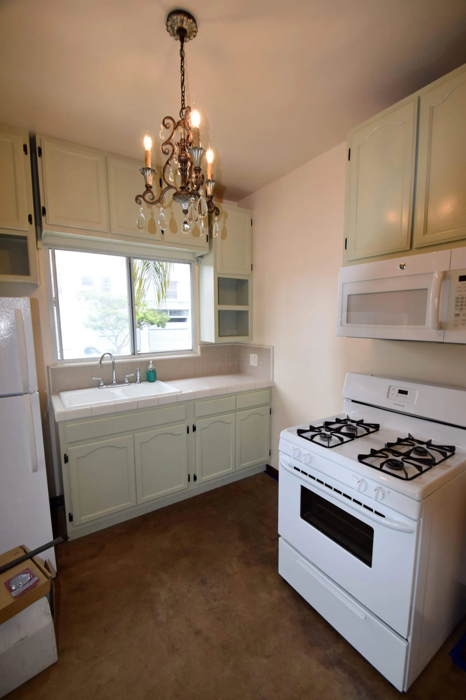 Renovated galley kitchen with sage cabinets, gas range, and chandelier in a Broadway Lofts unit