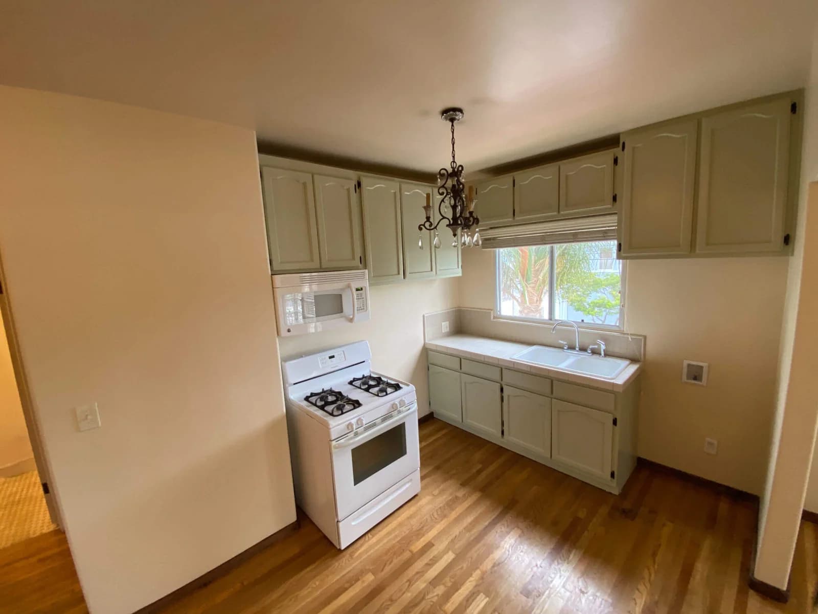 Compact kitchen with sage shaker cabinets and white appliances over hardwood flooring at Broadway Lofts
