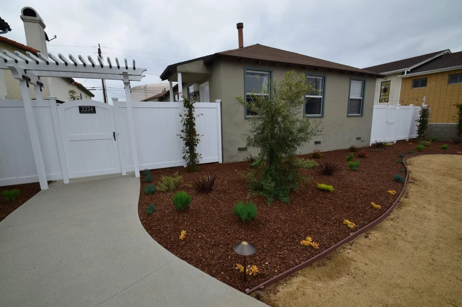 Cabrillo Bungalows front yard with white pergola gate and mulched, drought-tolerant garden beds