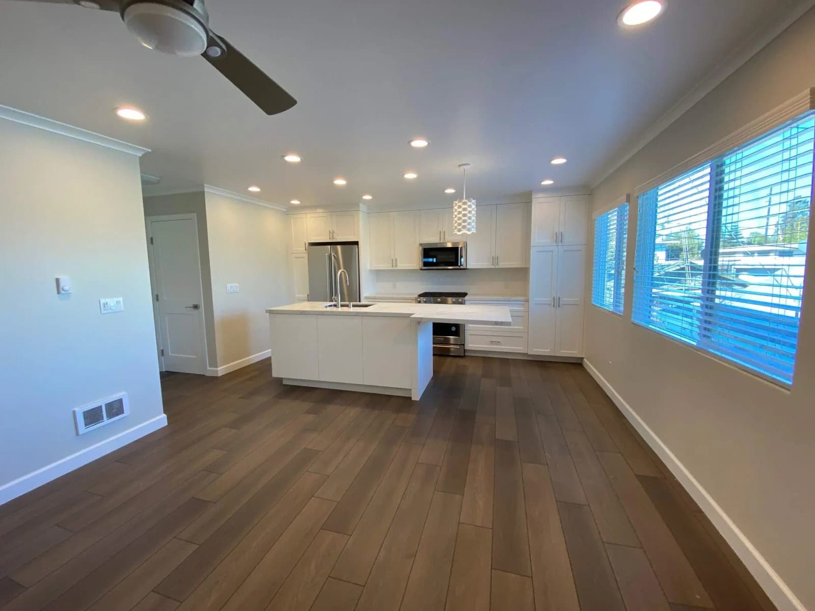 Open-concept Penmar Lofts kitchen and living area with white island, hardwood floors, and large windows
