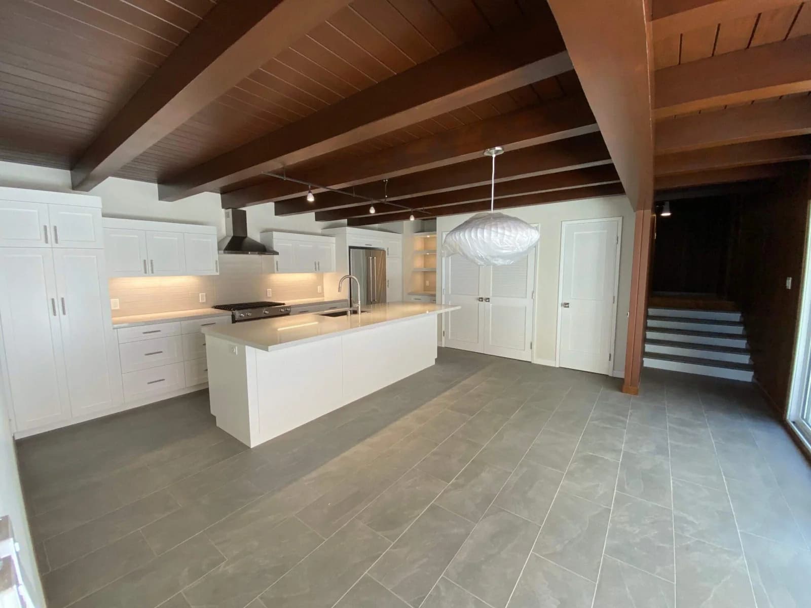 Open kitchen and living space with white cabinetry, beamed ceiling, and tile floor opening to a staircase in Redondo Beach