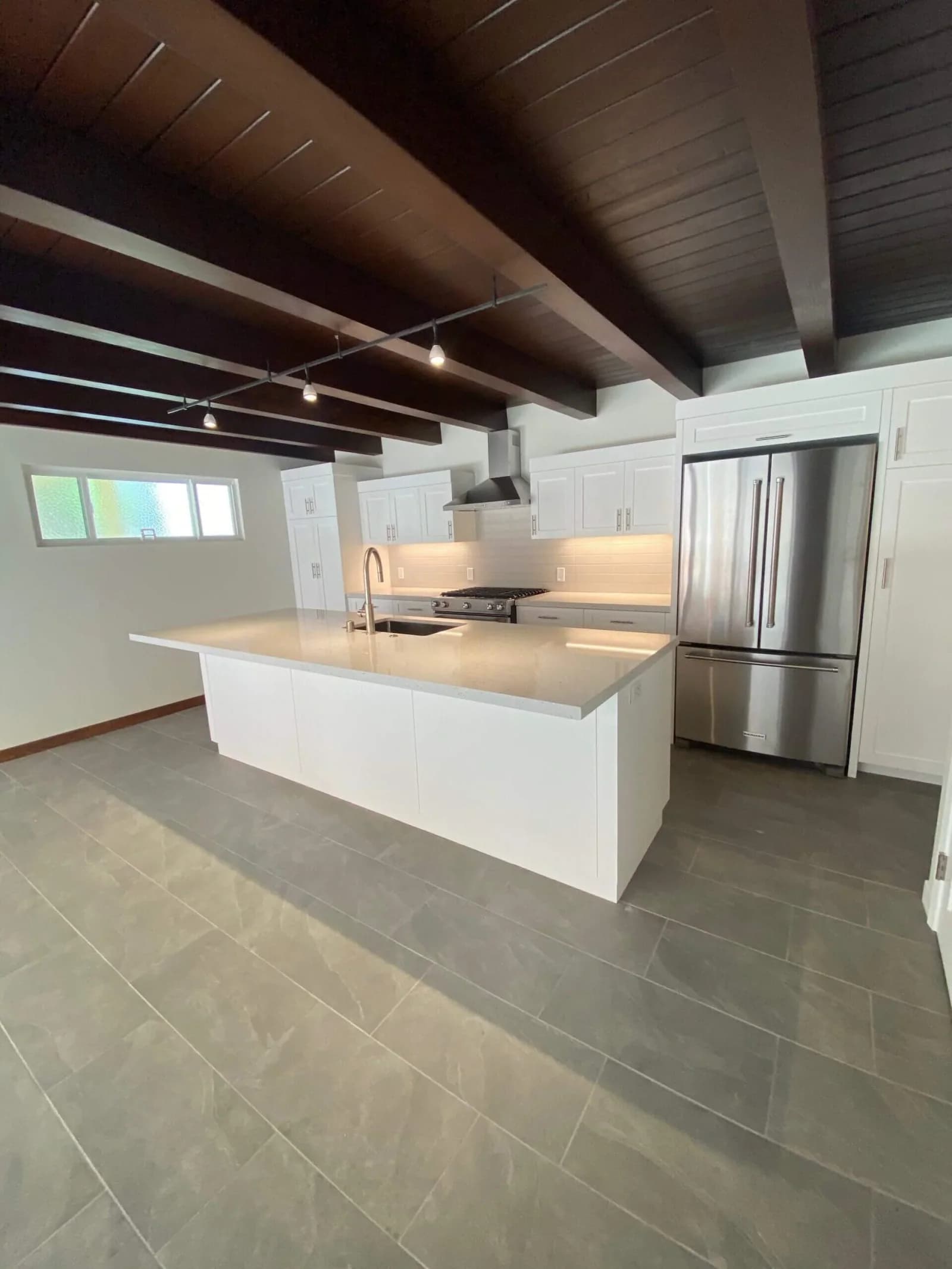 Spacious kitchen with long white island, stainless refrigerator, and dark beamed ceiling in Redondo Beach