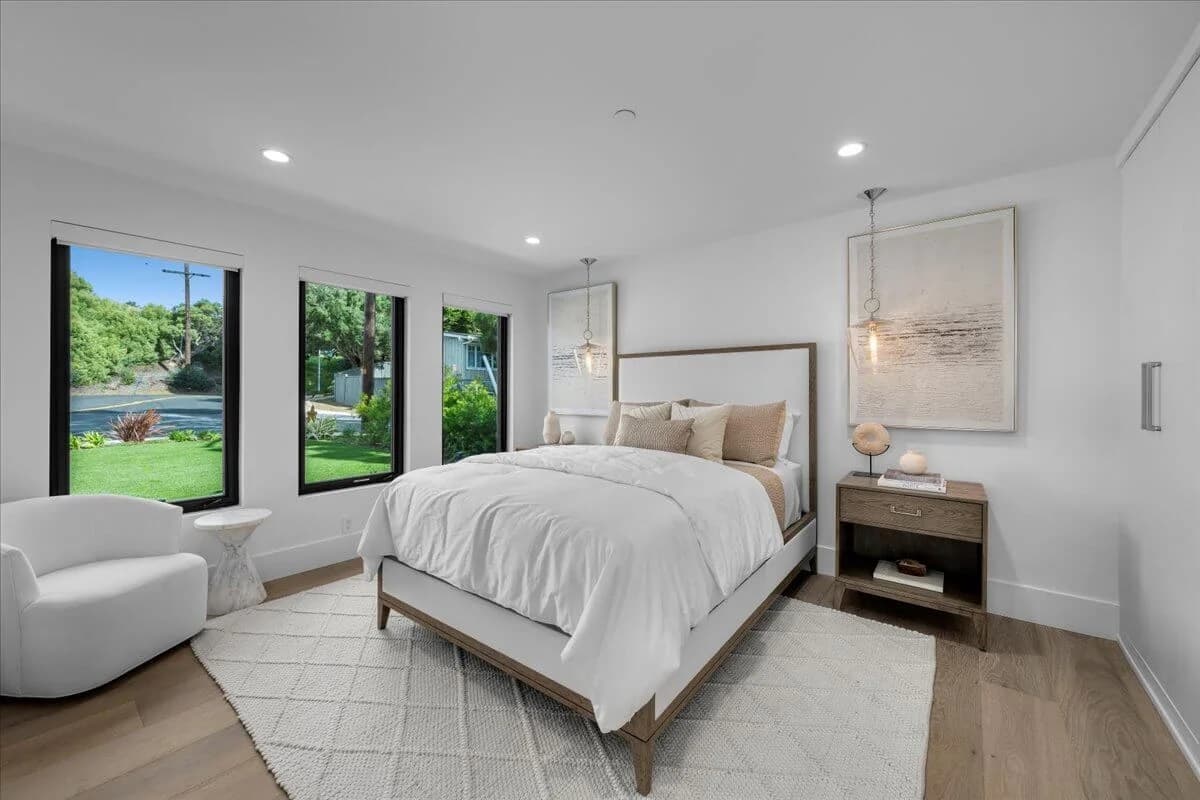 Bright primary bedroom with white oak floors, large windows, and upholstered platform bed