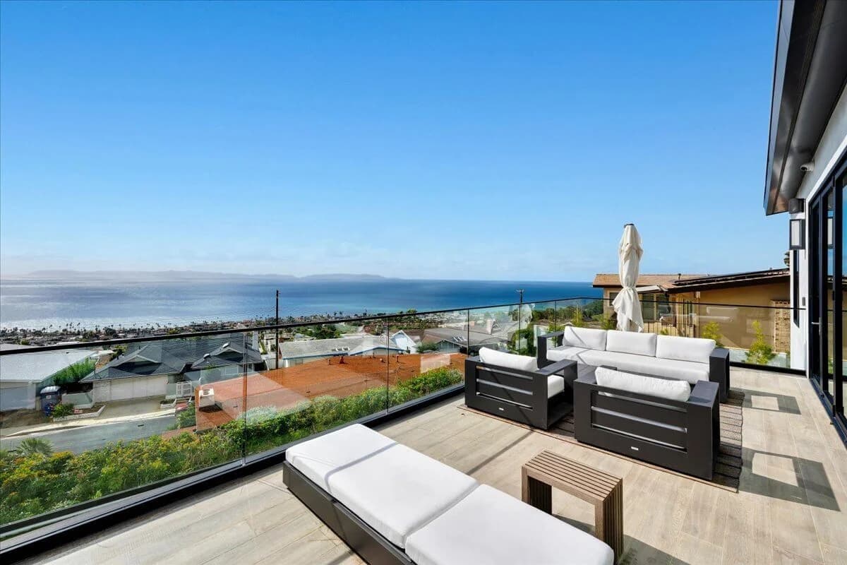 Glass-railed deck with lounge seating and sweeping Pacific Ocean and coastline views