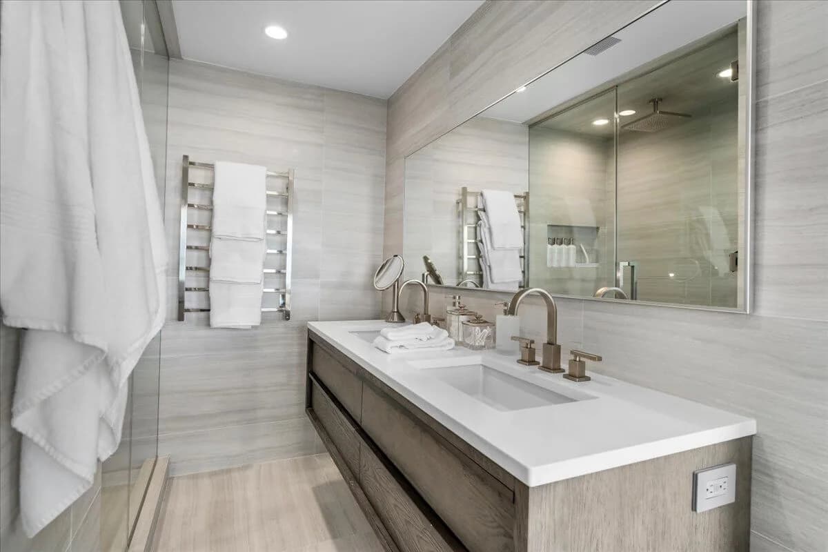 Spa bathroom with double vanity, heated towel rack, and large frameless mirror