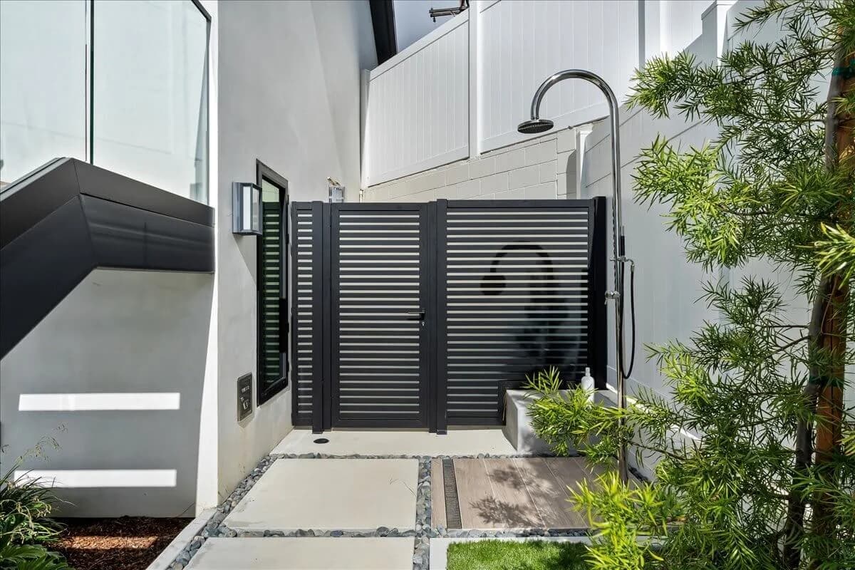 Side-yard outdoor shower with slatted privacy gate and modern stucco walls