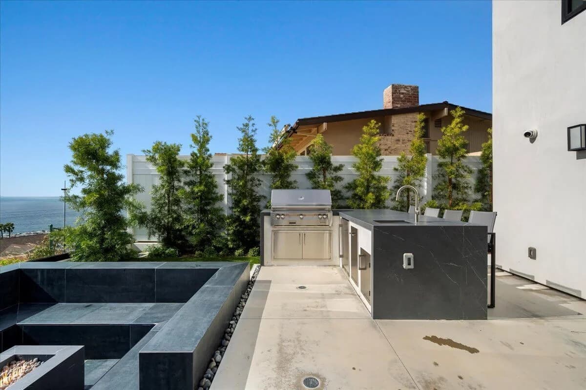 Outdoor kitchen with built-in grill, stone island, and bar seating near the ocean