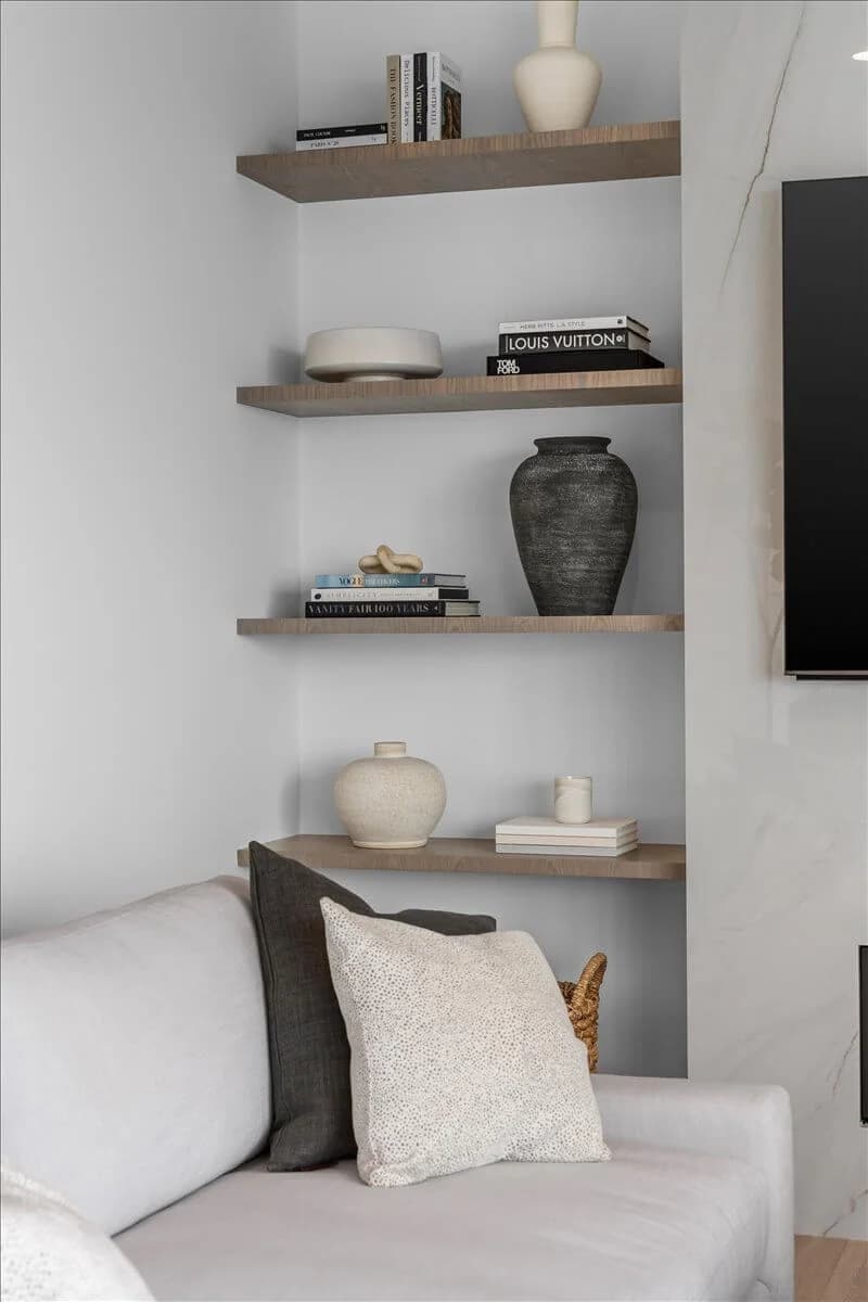 Built-in oak shelves styled with vases and books beside a marble fireplace surround