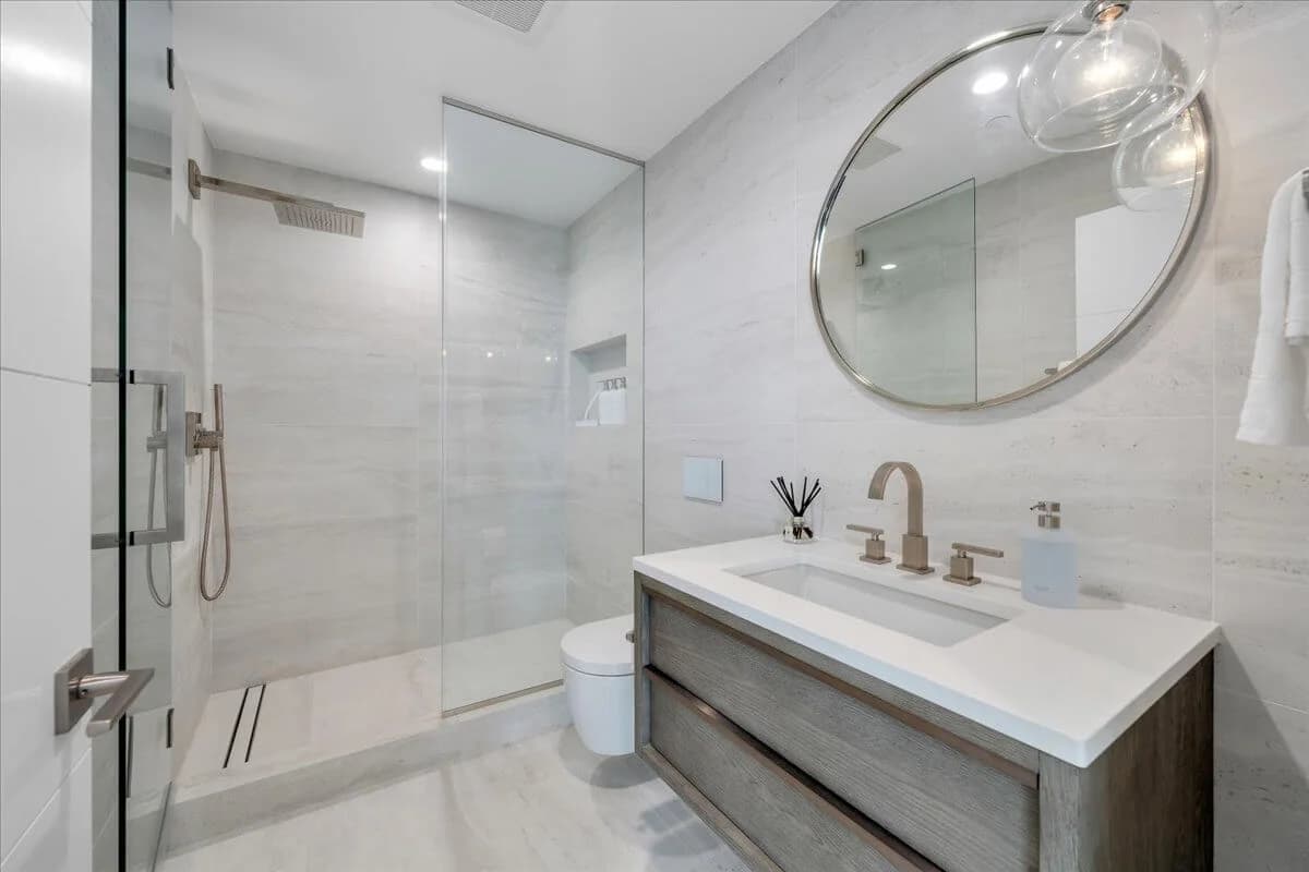 Modern bathroom with floating oak vanity, round mirror, and glass-enclosed shower