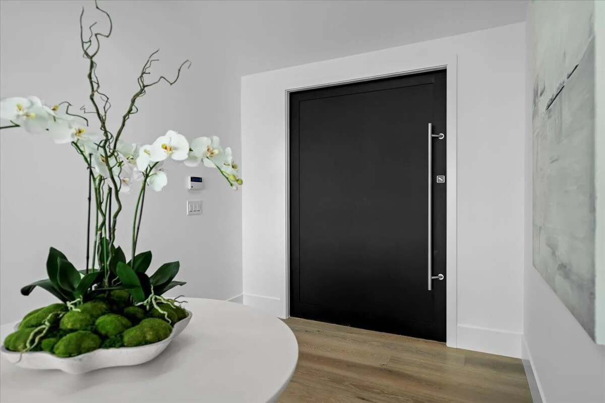 Matte black pivot front door framed by crisp white walls and wood flooring