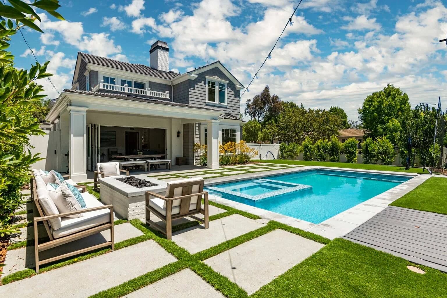Rectangular pool and spa with fire-pit seating and turf-lined pavers behind the home
