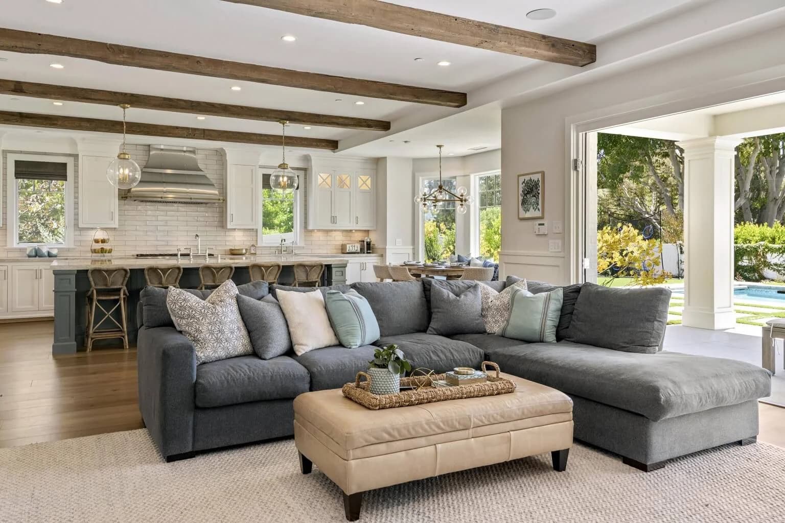 Family room sectional and ottoman beneath beamed ceiling, open to the farmhouse kitchen