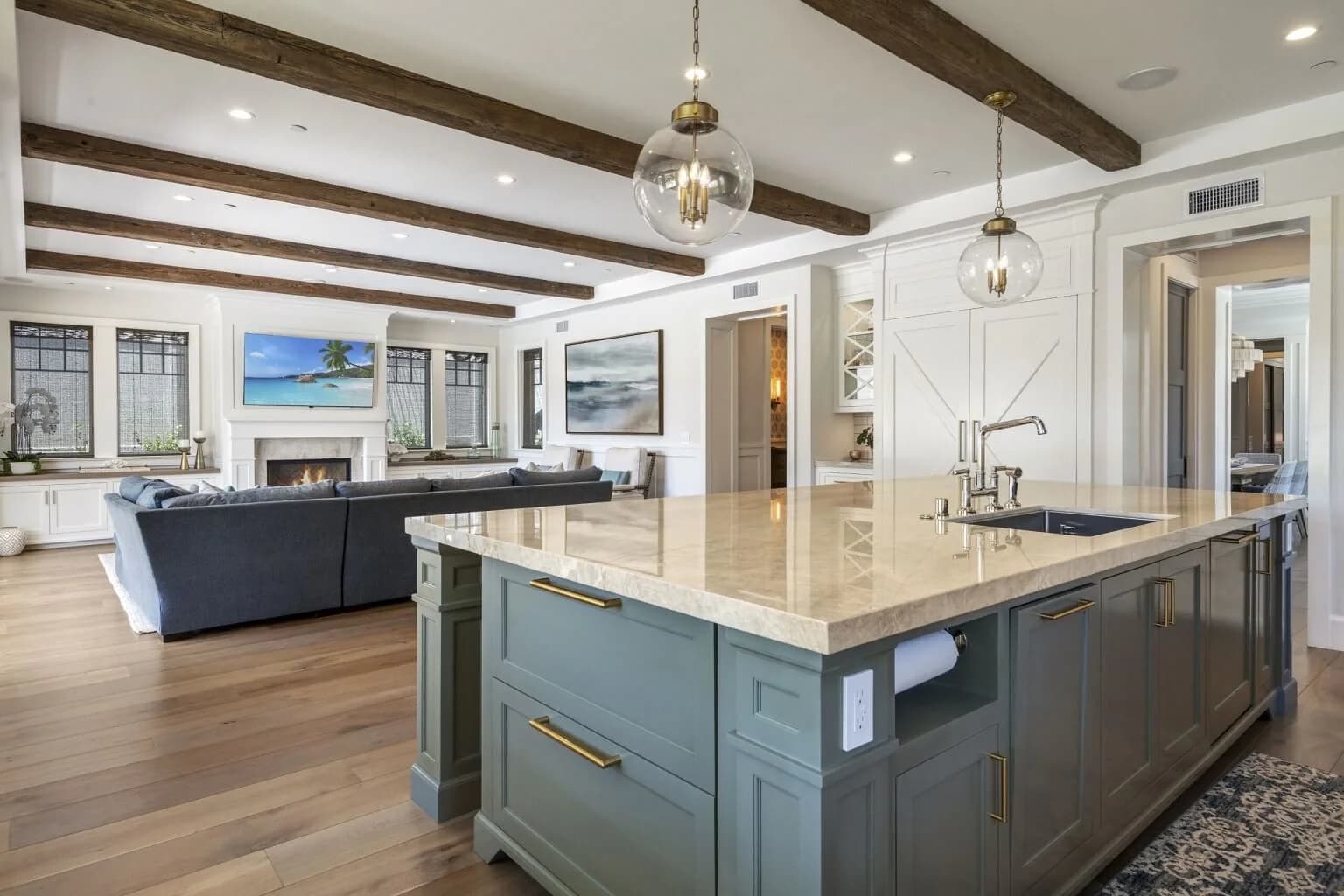 Kitchen island with marble top and prep sink, glass pendants, open to the beamed living room