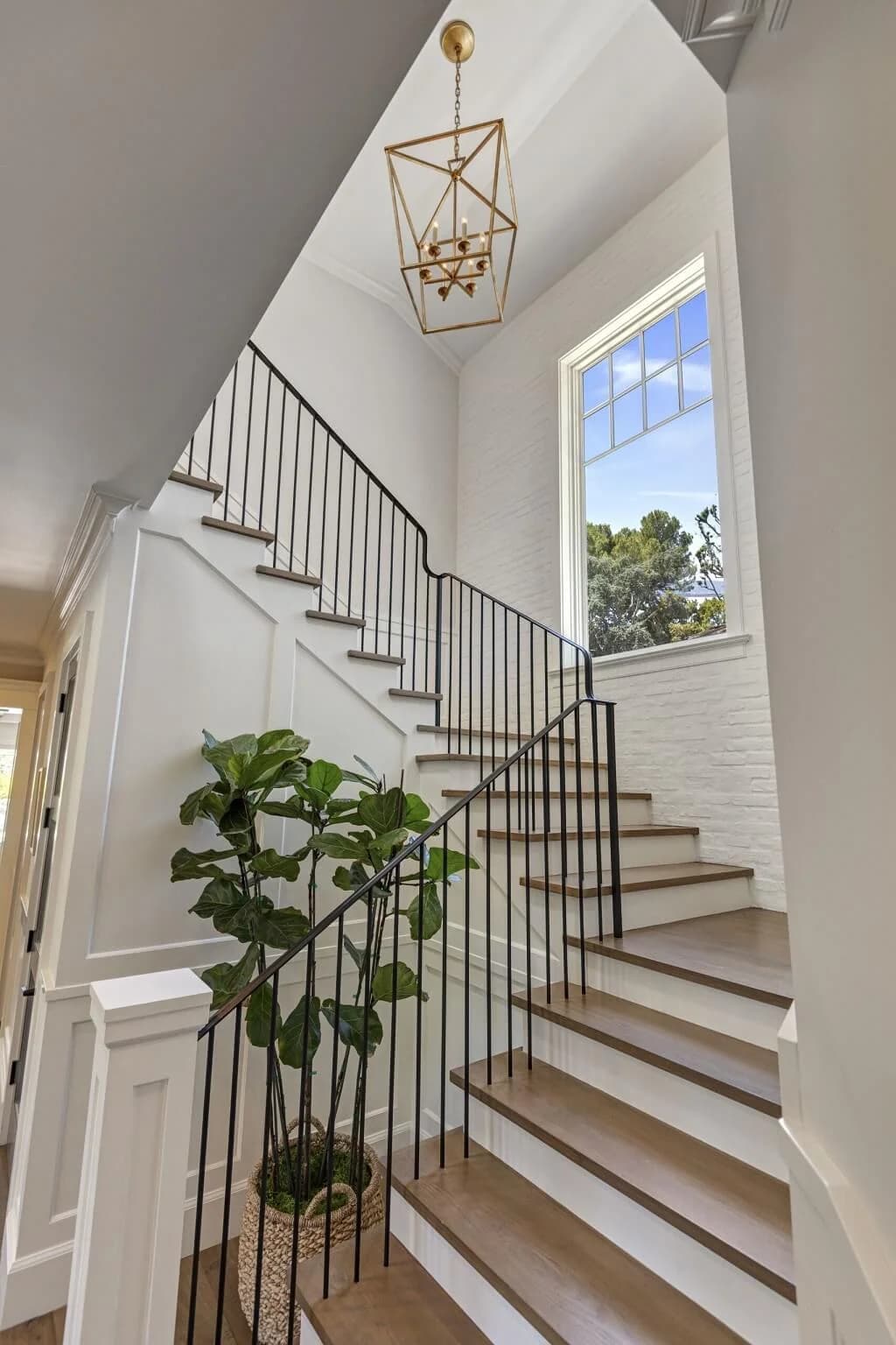 Staircase with iron balusters and lantern pendant beside a painted brick wall and window