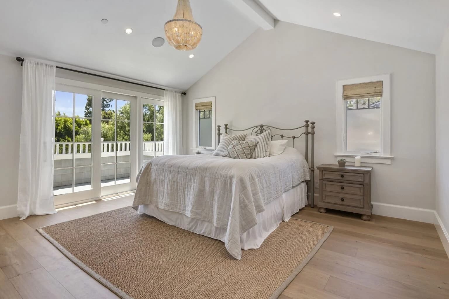 Primary bedroom with vaulted ceiling, four-poster bed, and balcony doors to a deck