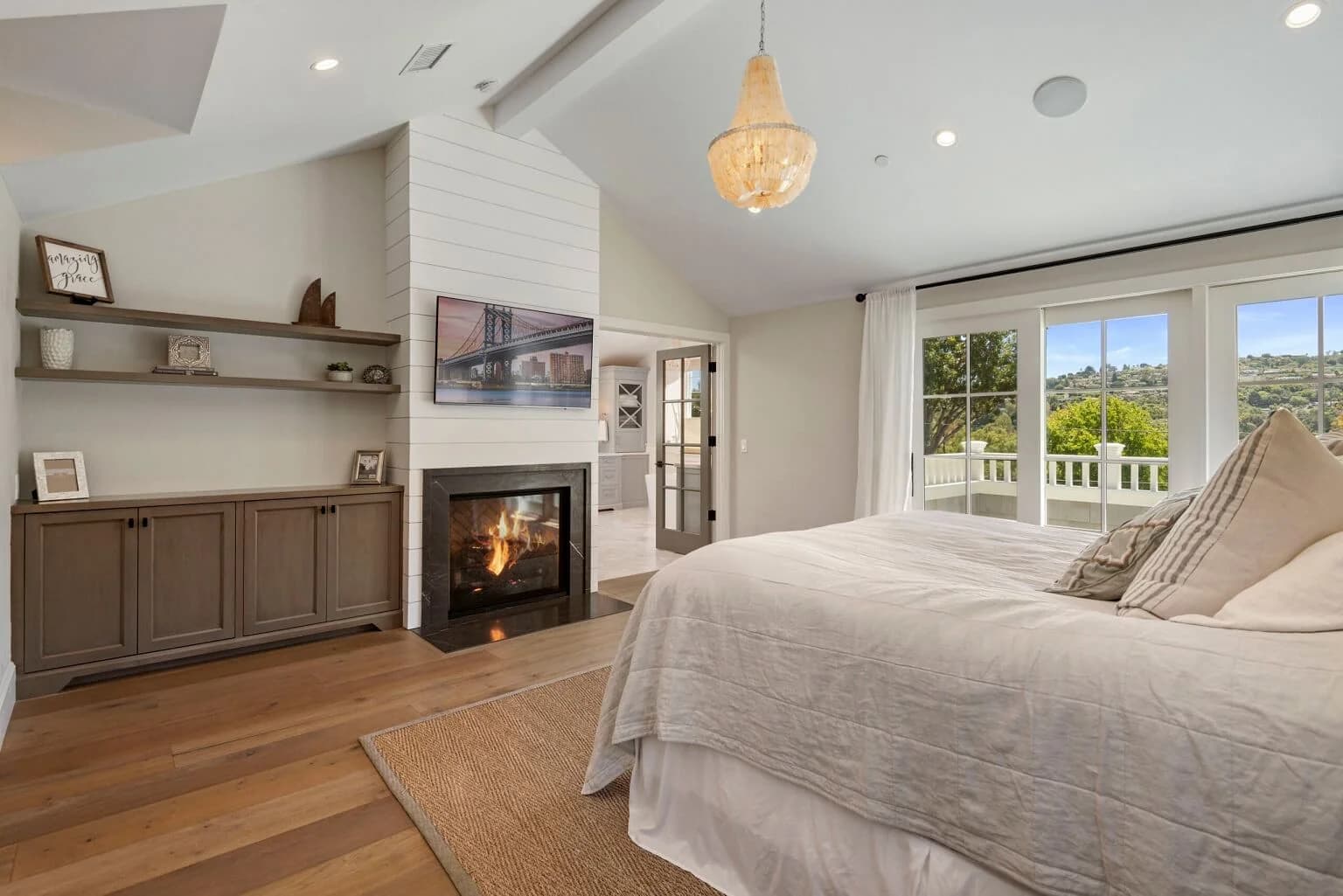 Primary suite with shiplap fireplace, built-in shelving, and French doors to a hillside-view balcony