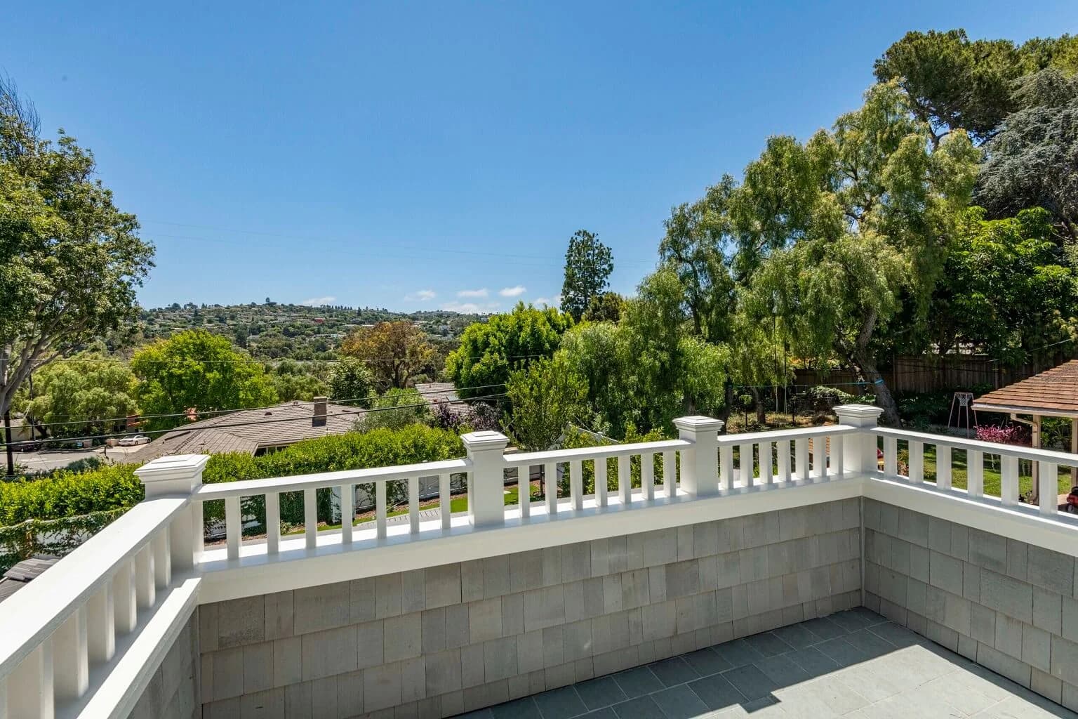 Private balcony with white railing overlooking treetops and rolling Palos Verdes hills