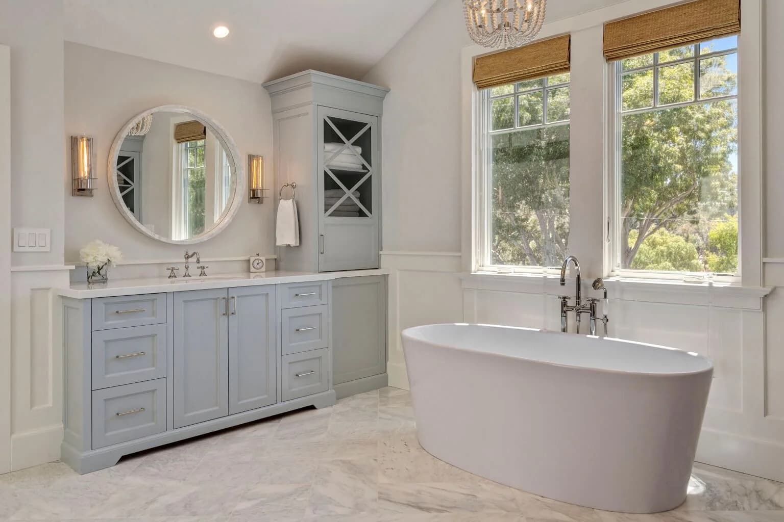 Spa-style bath with light blue vanity, round mirror, and soaking tub beneath windows