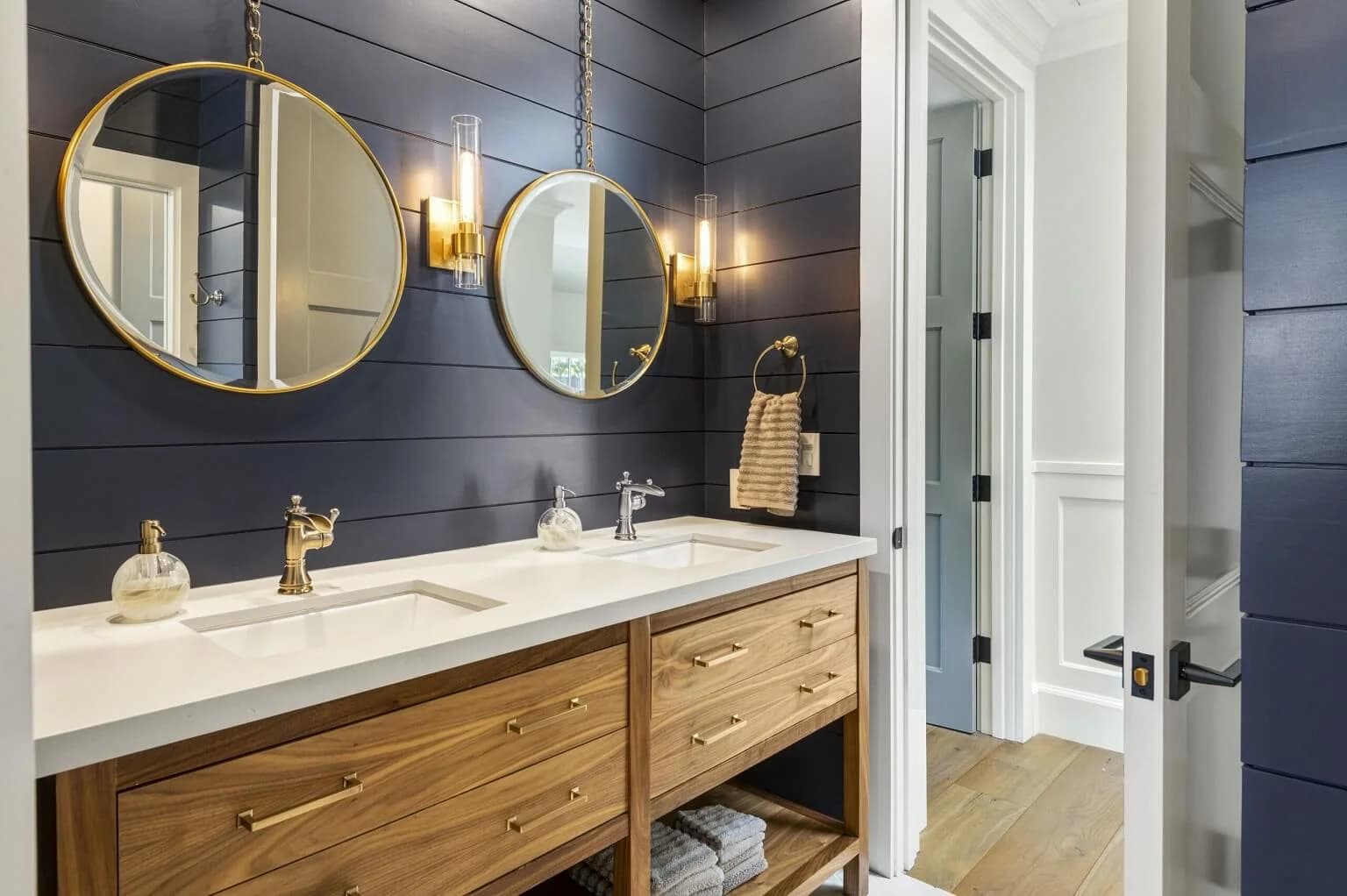 Bathroom with navy shiplap walls, twin round gold mirrors, and a walnut double vanity