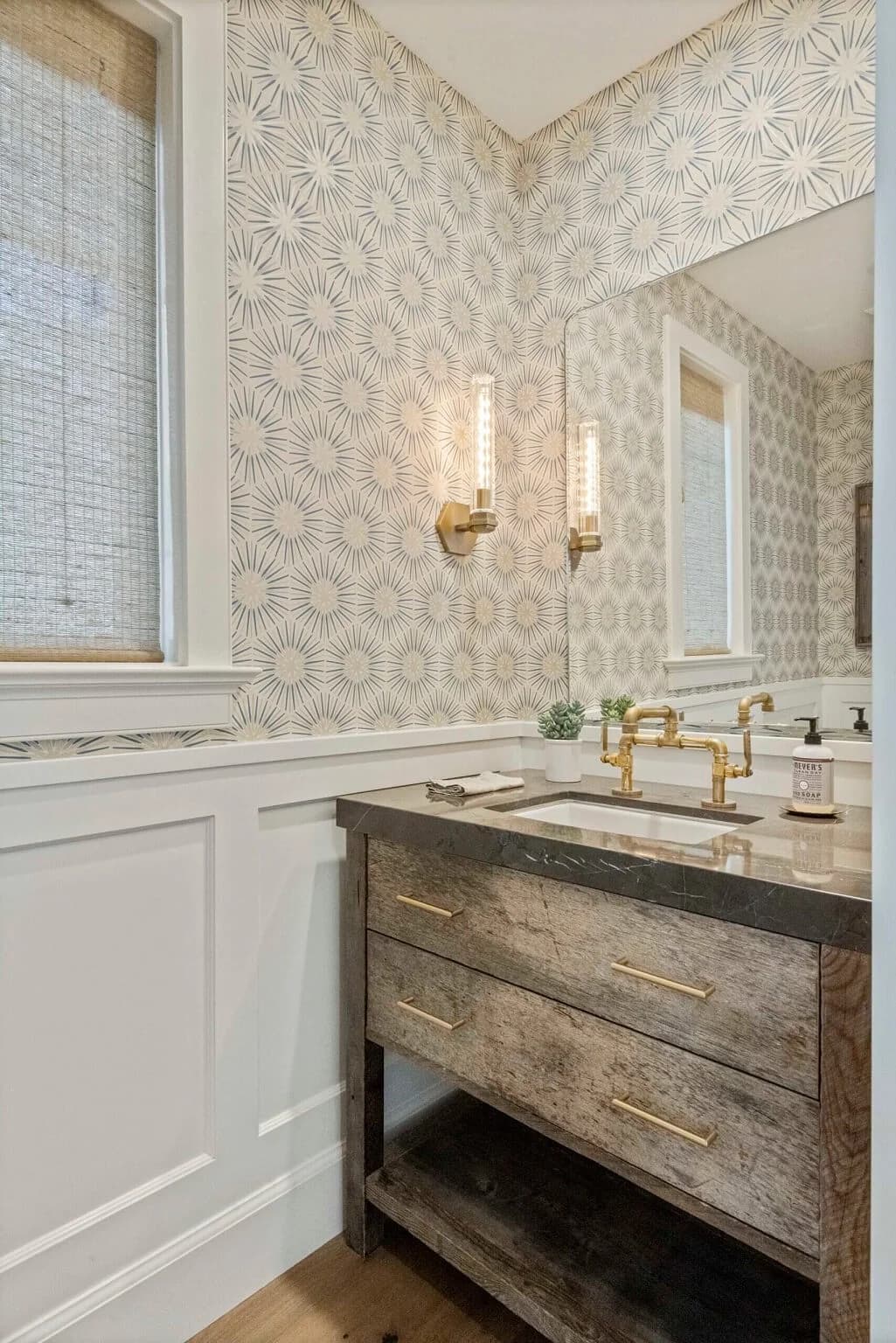 Powder room with patterned wallpaper, reclaimed-wood vanity, and brass sconces