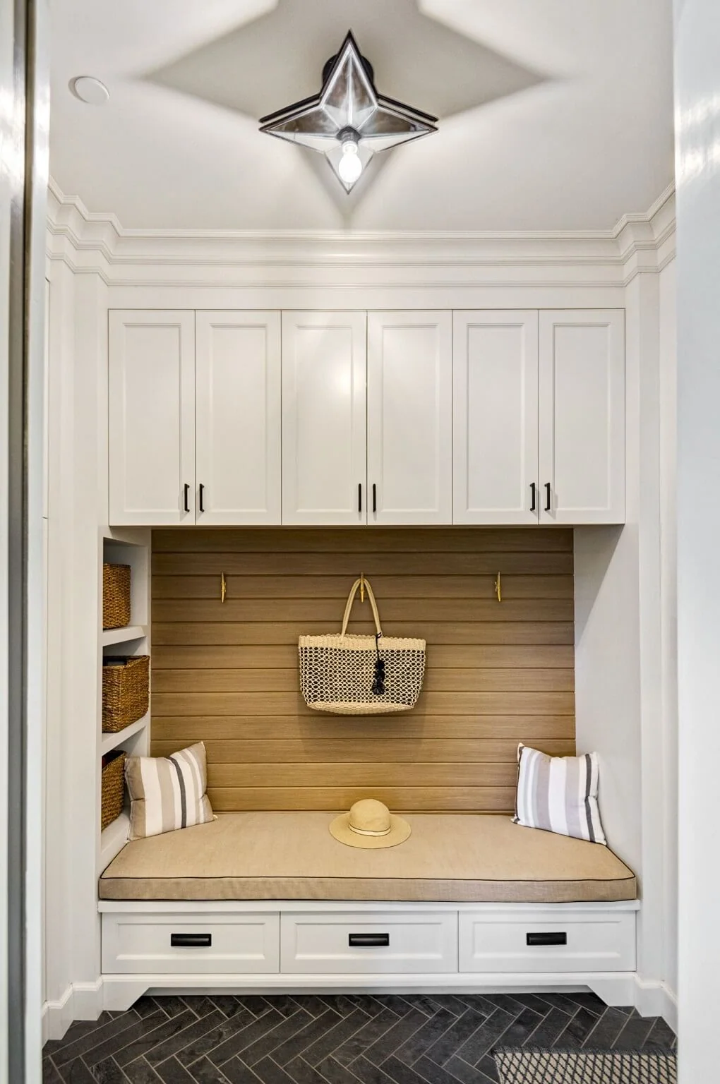 Mudroom built-in with white cabinets, cushioned bench, woven baskets, and star pendant light
