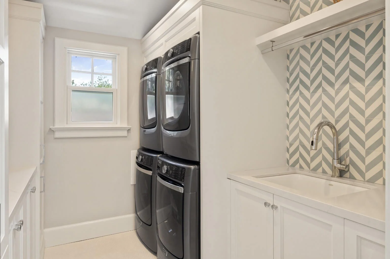 Laundry room with stacked washers and dryers, utility sink, and chevron-tile backsplash